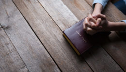 hands praying with a bible in a dark over wooden table