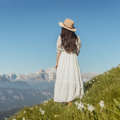Young woman standing in flowers field on hilltop looking at mountain scenery